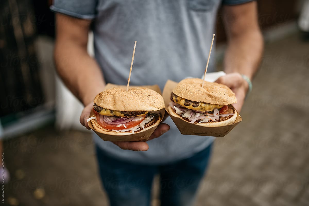 Crop person holding hamburgers on street