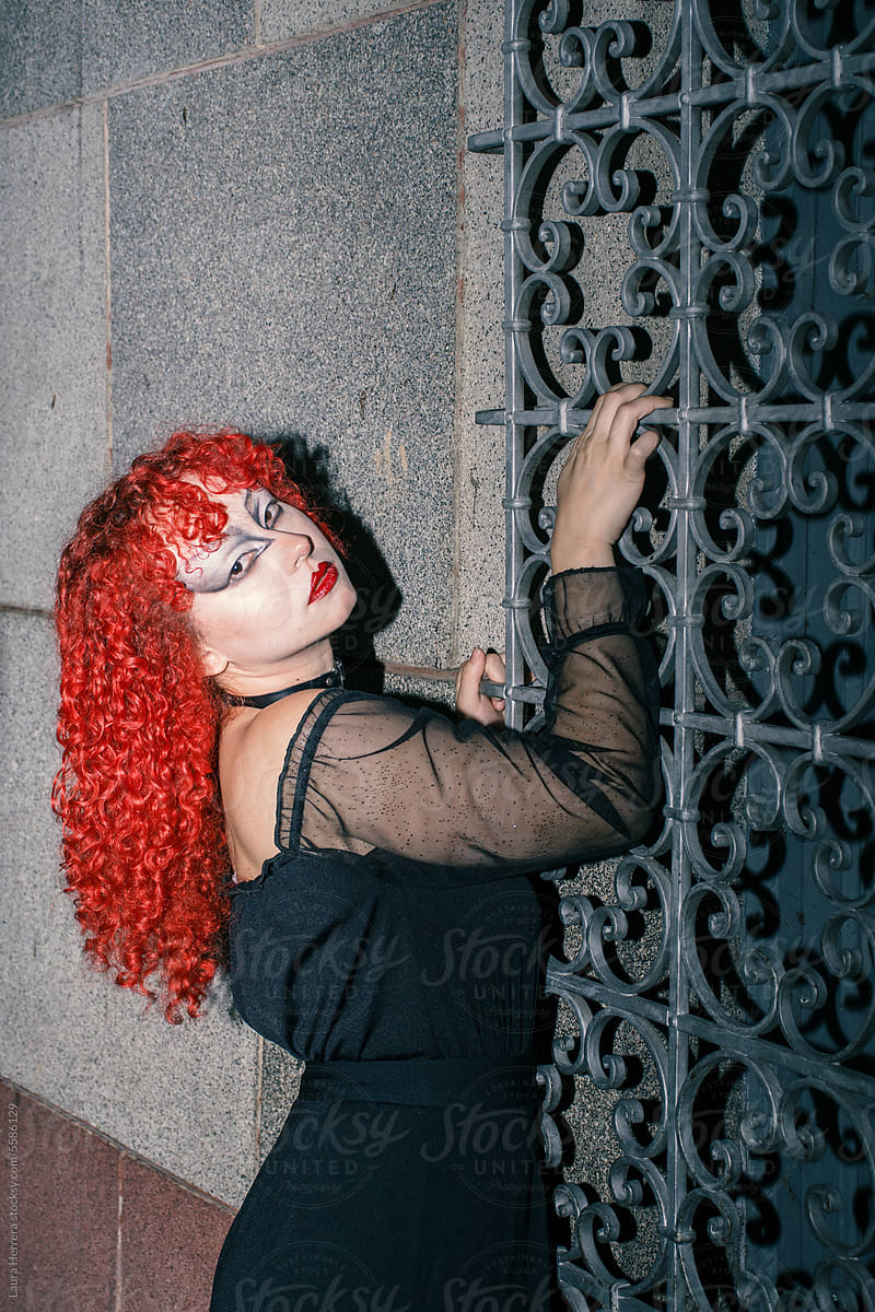 Gothic curly redhead poses on a gothic window grill