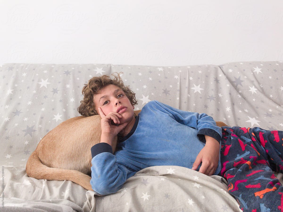 Boy lying over dog's back on sofa