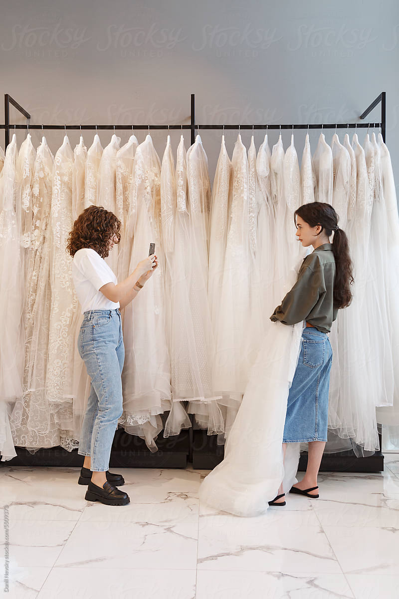 Friend taking photo of bride with wedding gown at shop