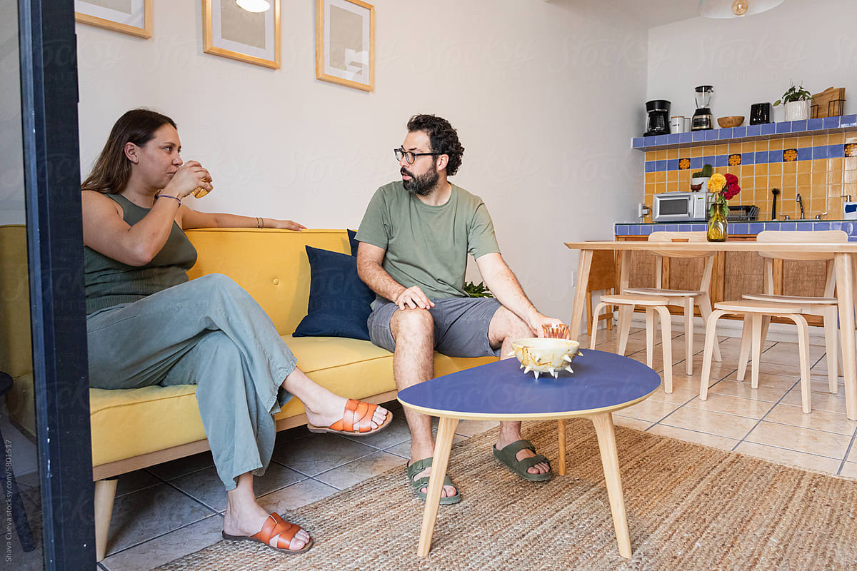 Couple talks while sitting on a yellow sofa with a rug on the floor
