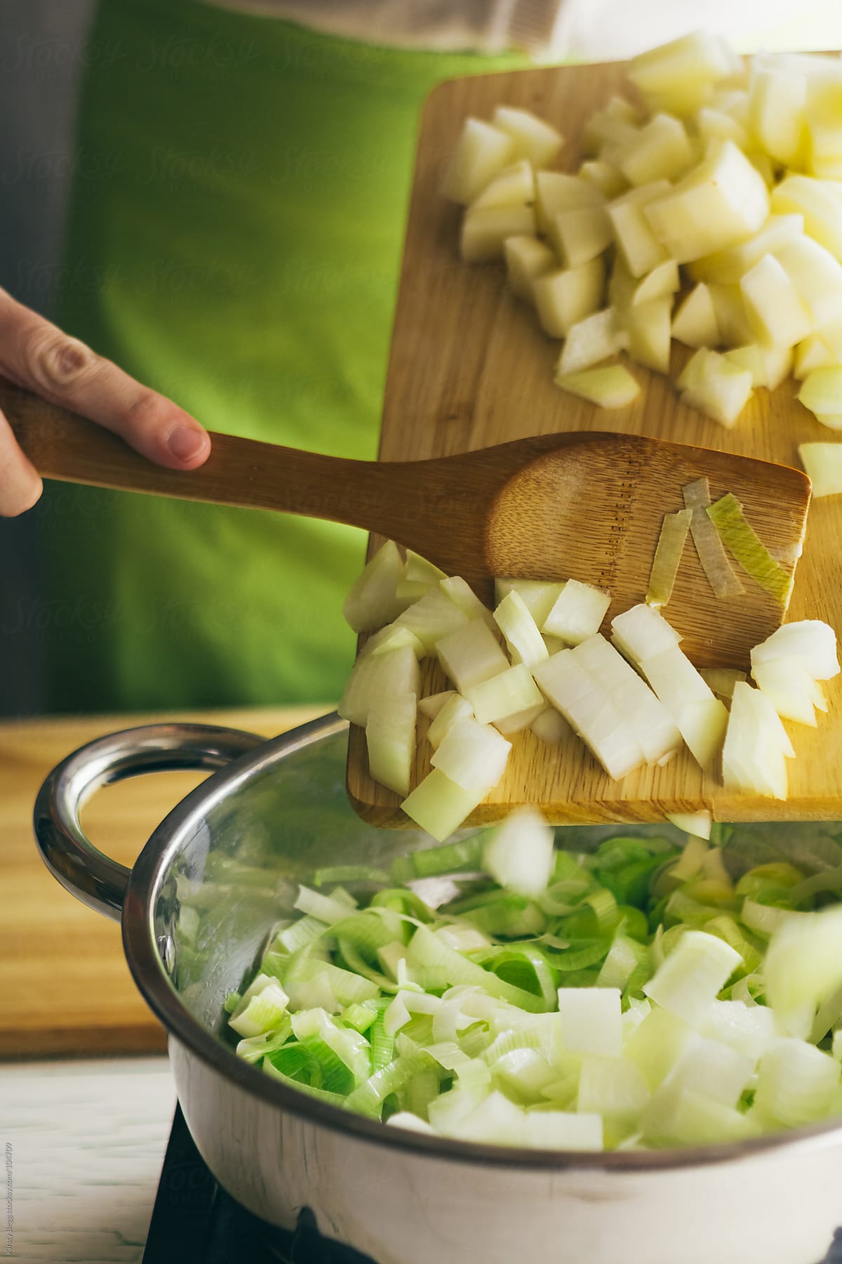 Woman tipping diced onion and potato into saucepan of leeks