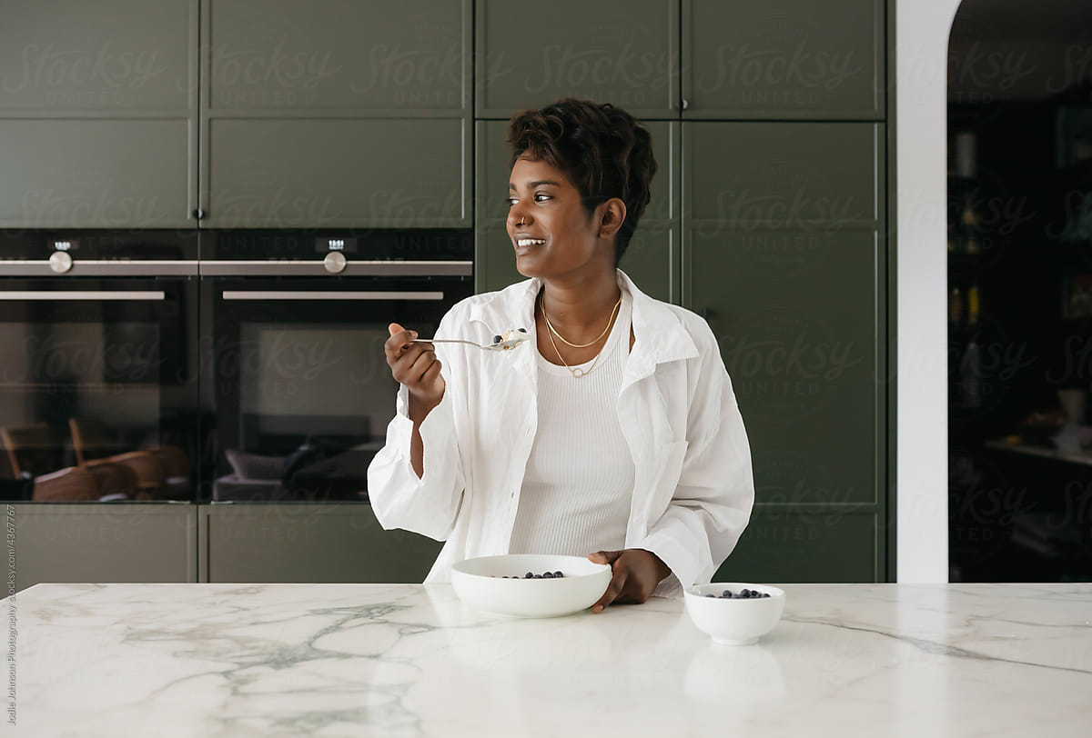 A mixed race woman eating cereal at her kitchen counter