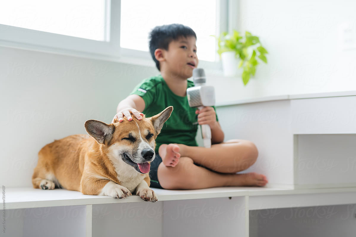 Happy boy singing karaoke with corgi dog near window