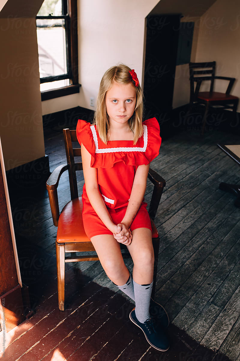 Girl in red dress sitting in chair.