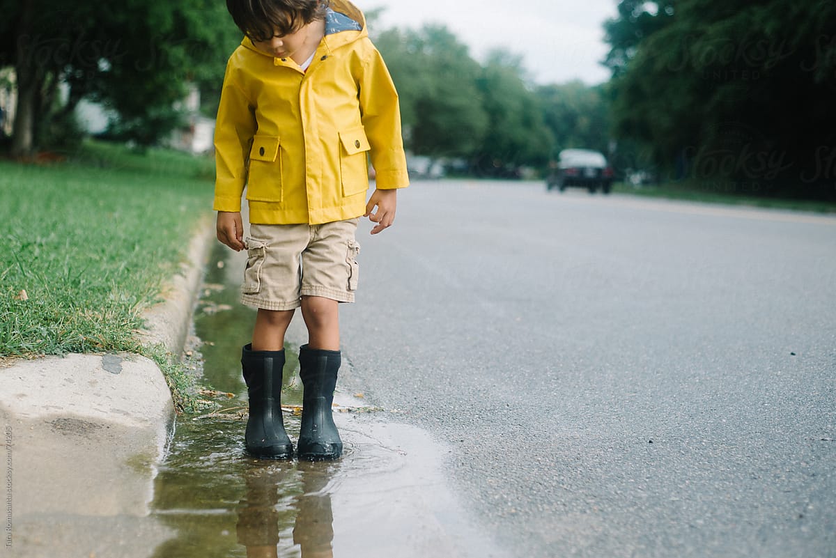 boy in rain jacket stands in a puddle