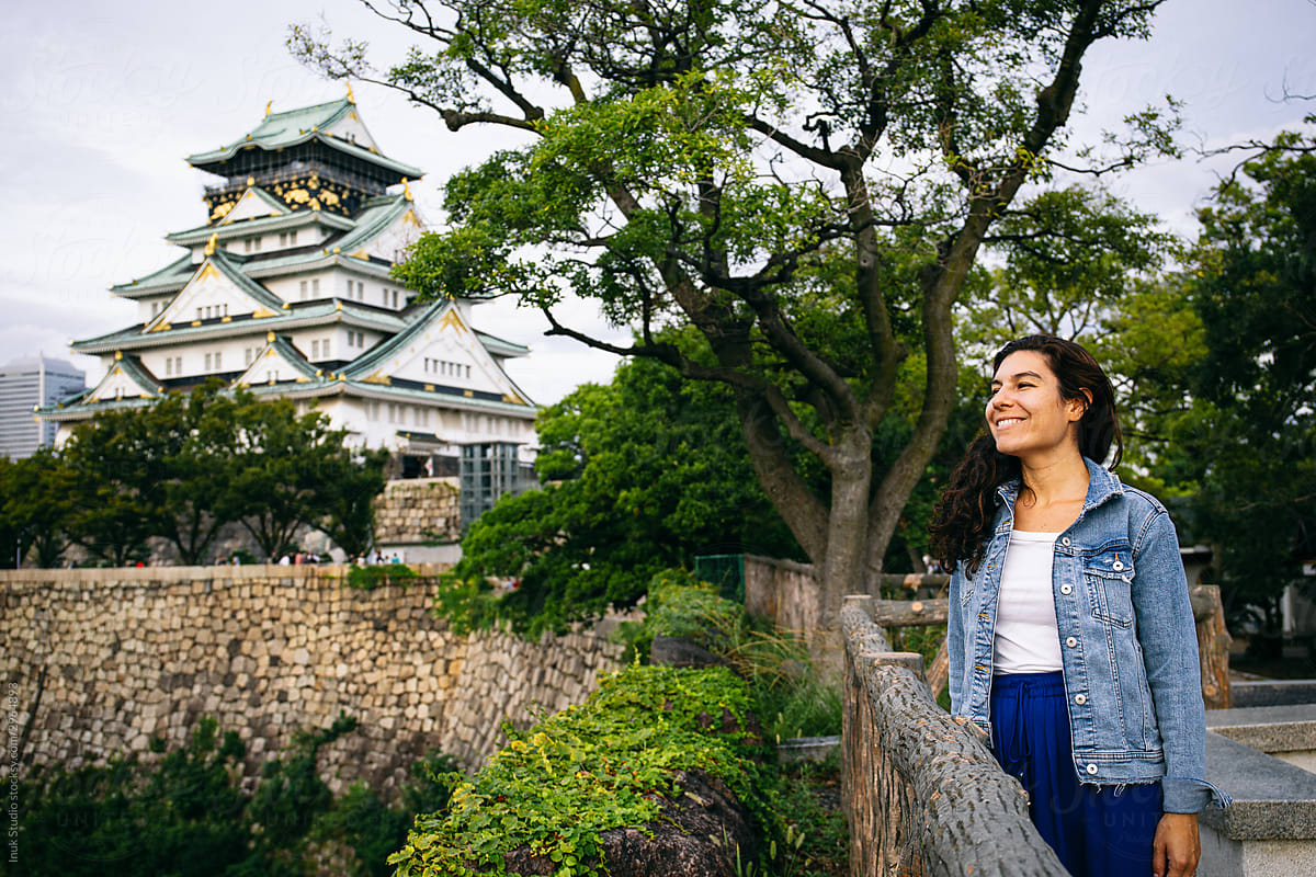 Delighted female traveler standing on bridge next to castle  building