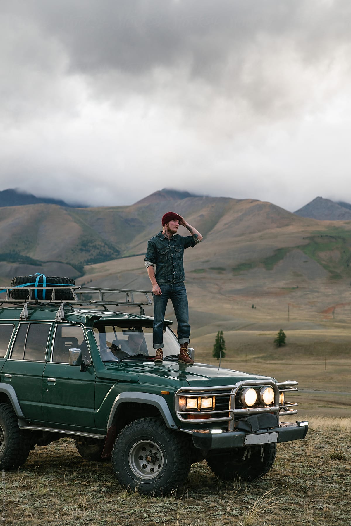 Young man standing on the old green jeep parked in wild area