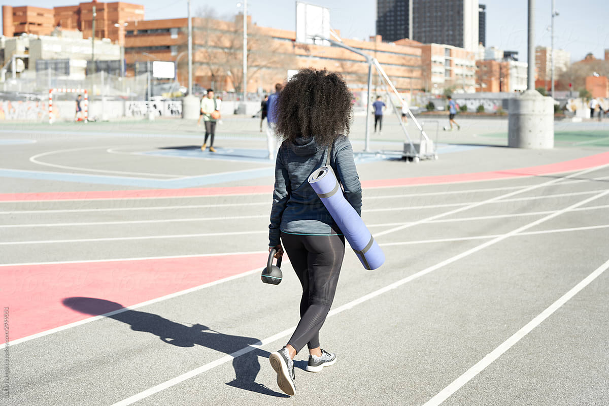 Black girl carrying kettlebell on sports ground