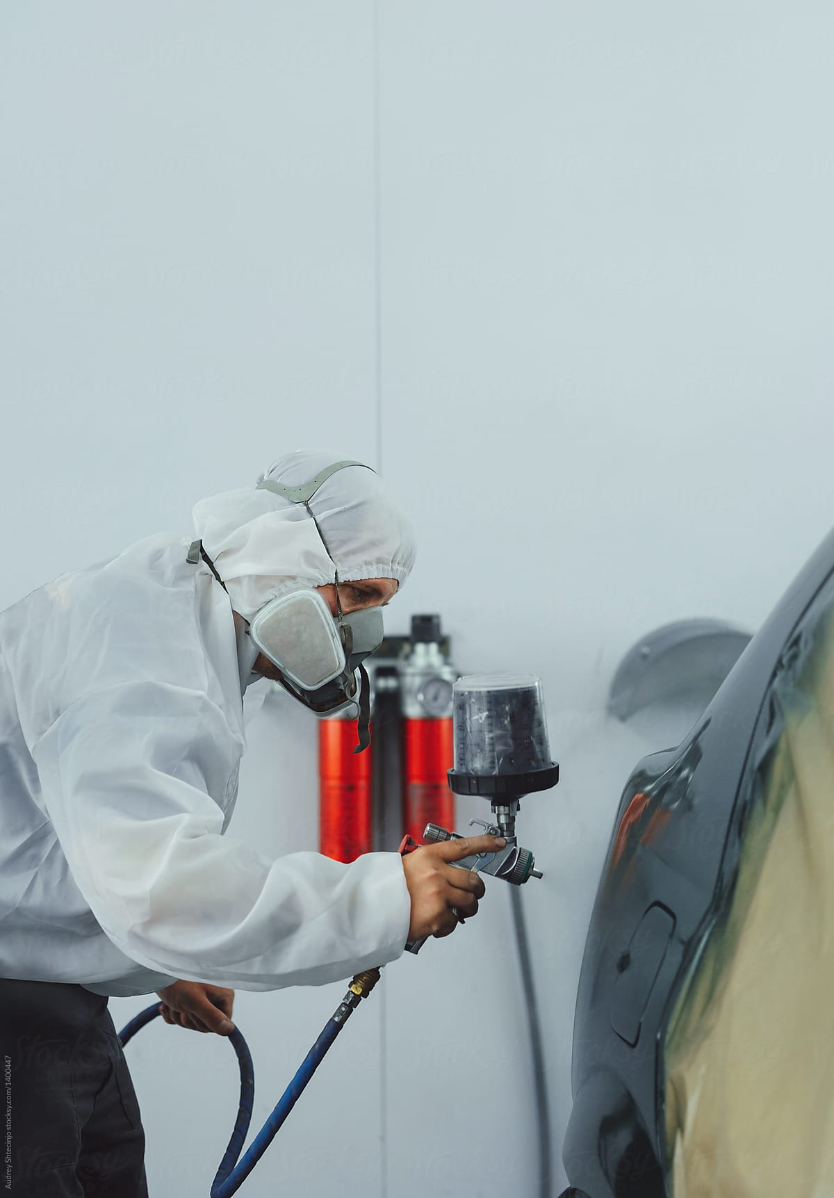 Worker/painter working on car bodywork in paint chamber/workshop.