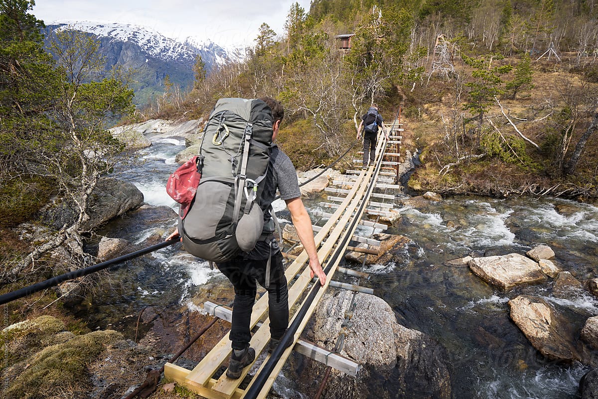 two males crossing a river on a suspension bridge while hiking in Norway.