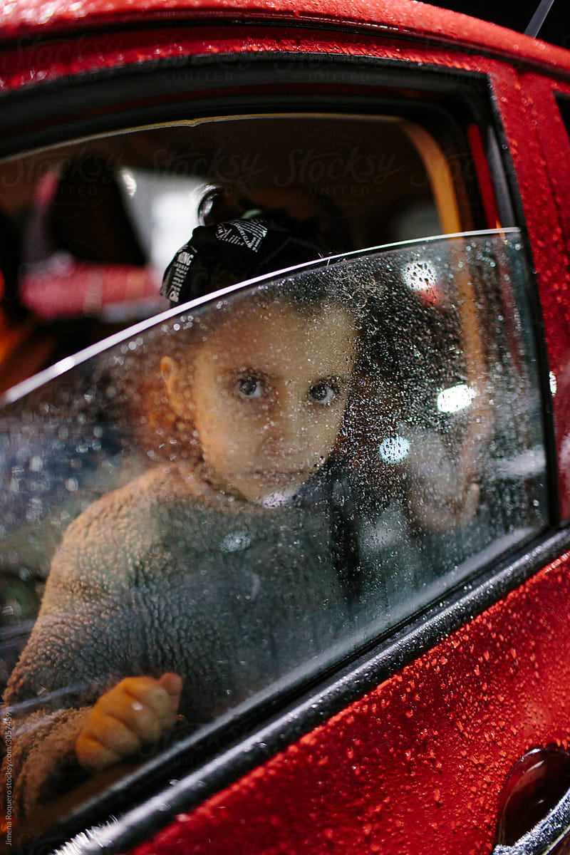 Kid in the rain inside a car looking at camera