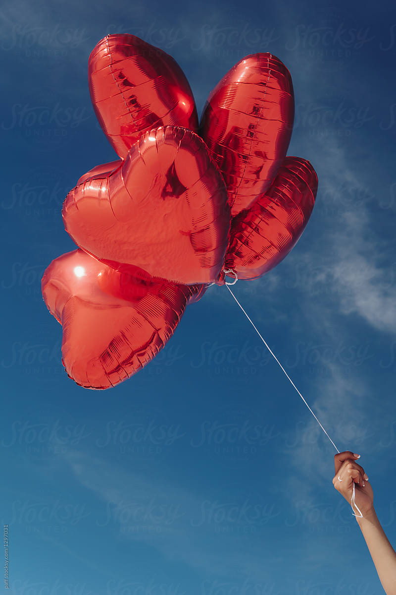 Girl\'s hand holding heart balloons on Valentine\'s Day outdoors