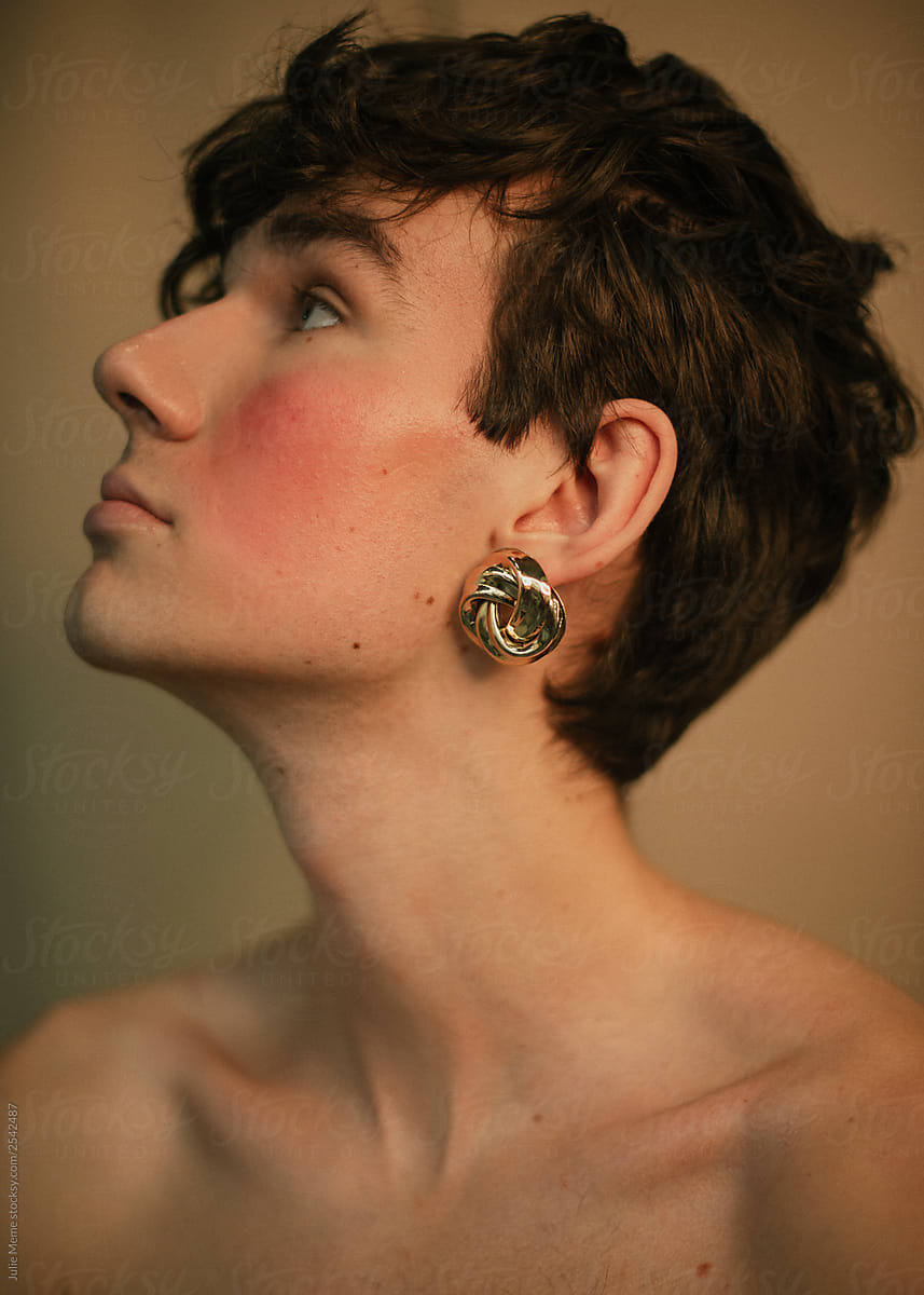 Portrait of a queer guy with curly hair and golden earrings without clothes