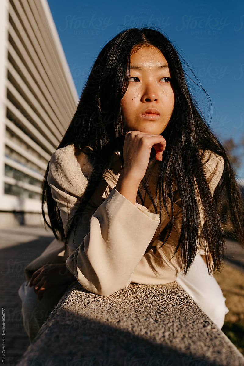 Dreamy Asian woman looking away on street in sunlight