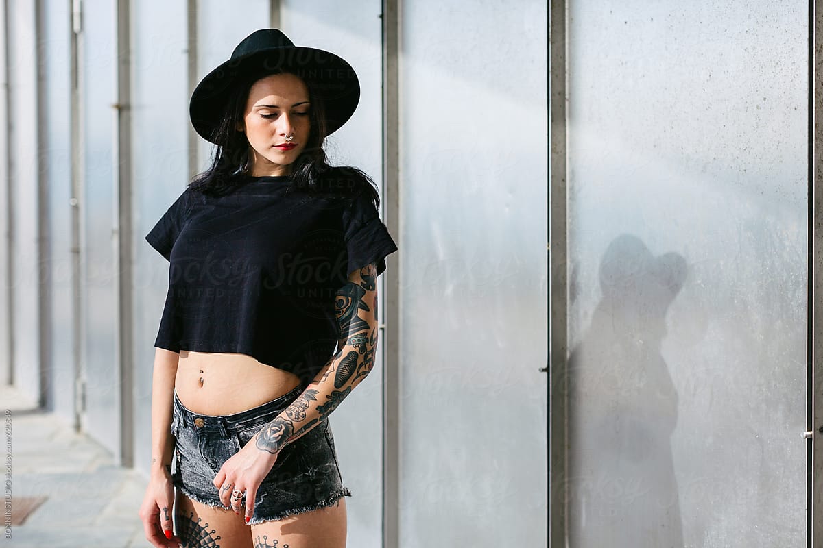 Young alternative woman with tattoos standing in front a wall.