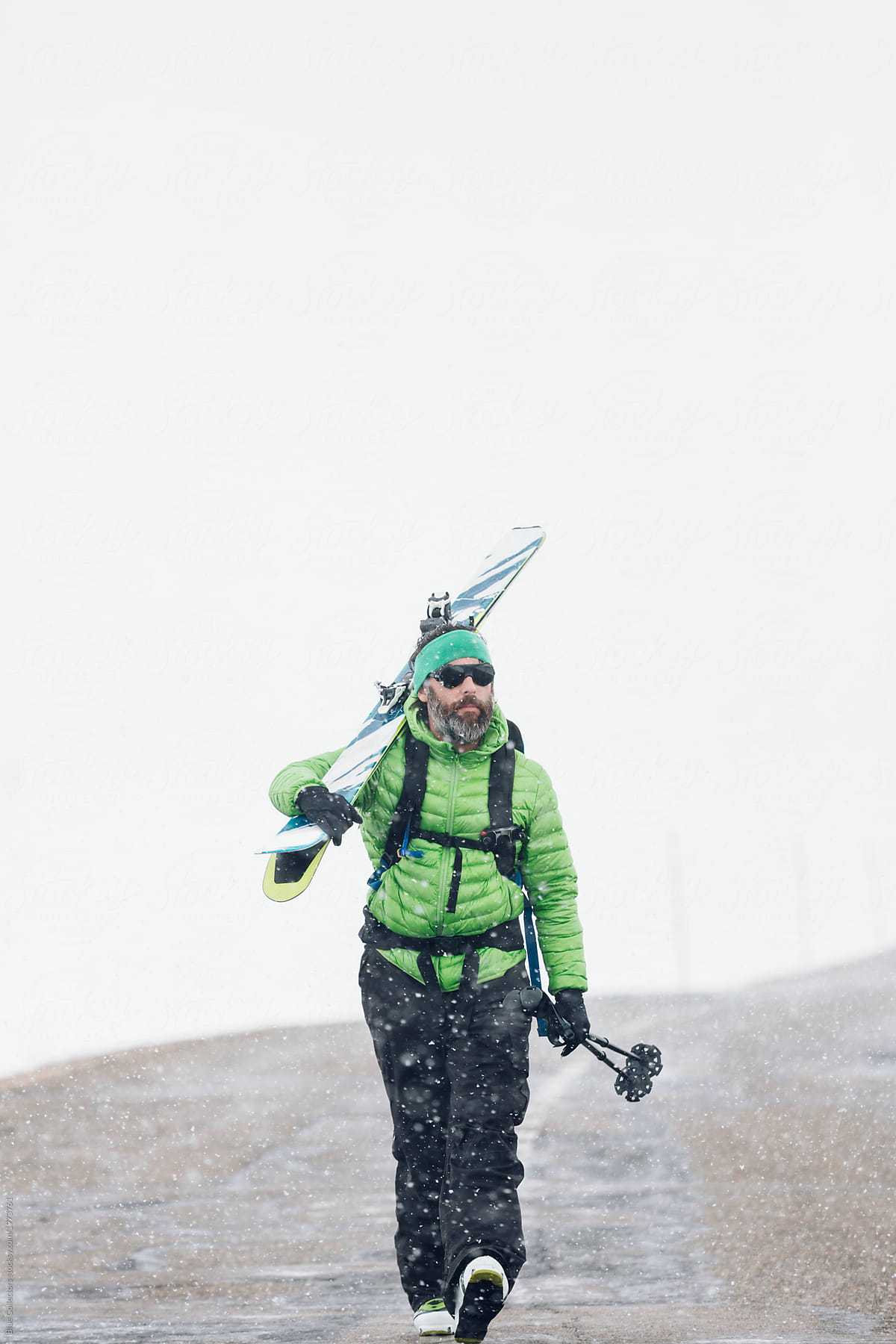 Skier walking along empty road in the snowy mountains in winter carrying skis