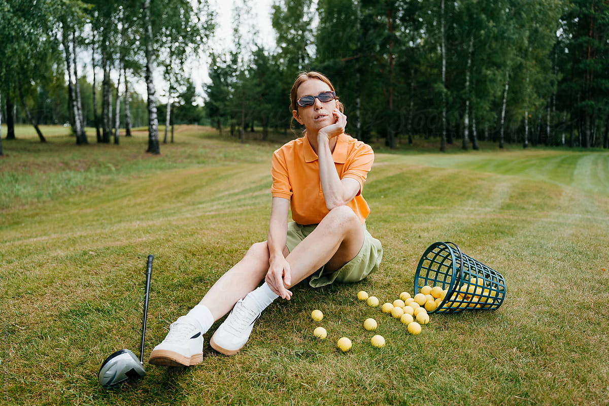 A woman is sitting on the lawn next to the golf equipment