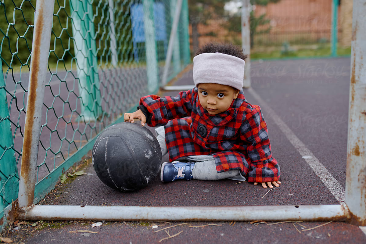 little girl in autumn clothes playing with a black basketball on the Playground