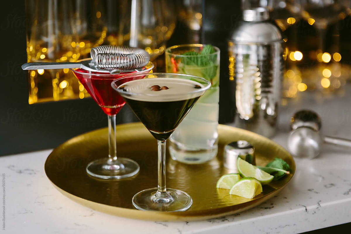An espresso martini on a brass tray with other drinks