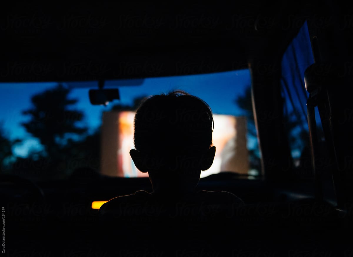 Child sits in the car watching a movie at a drive-in movie theater