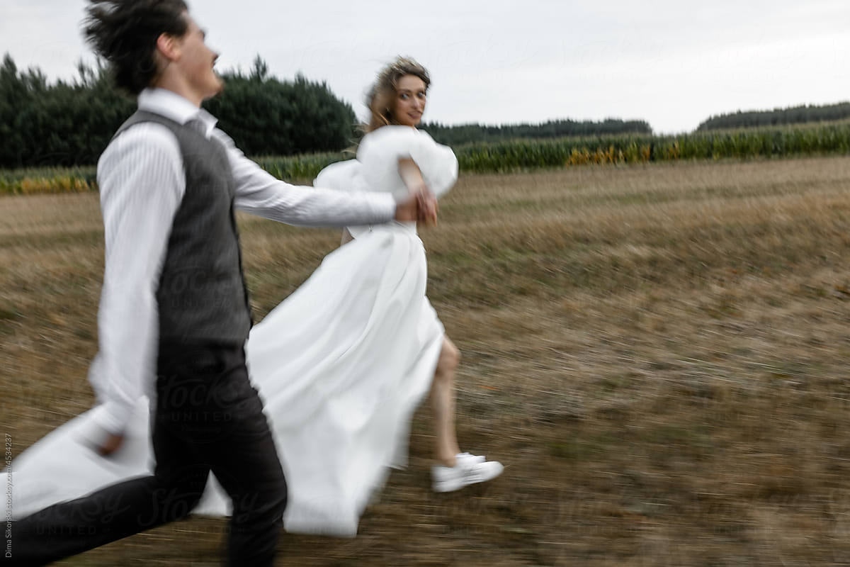 The bride and groom are running happily in motion across the field