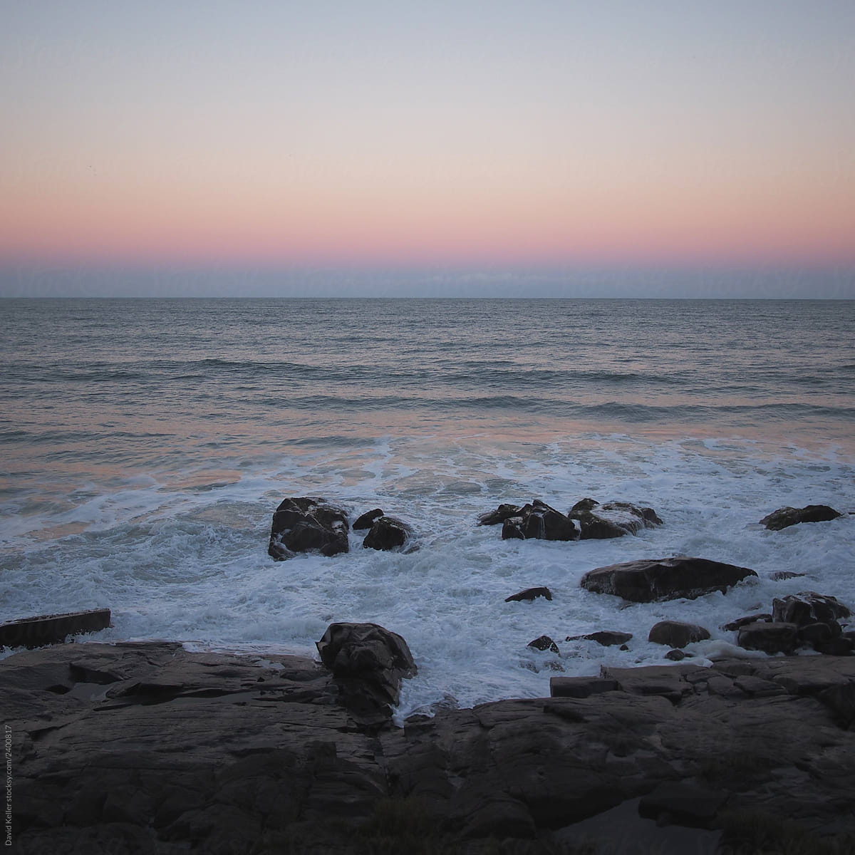 An purple sunset meets the water on a rocky coastline