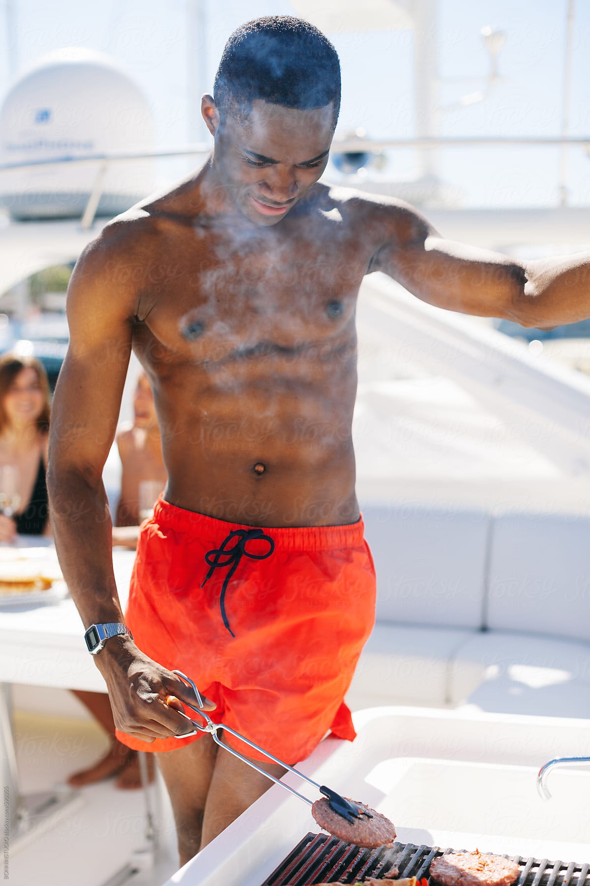 Young african american man cooking meat in a grill on a luxurious yacht.