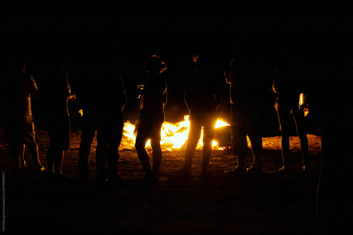 Silhouettes of a group of friends gathering around the fire at night