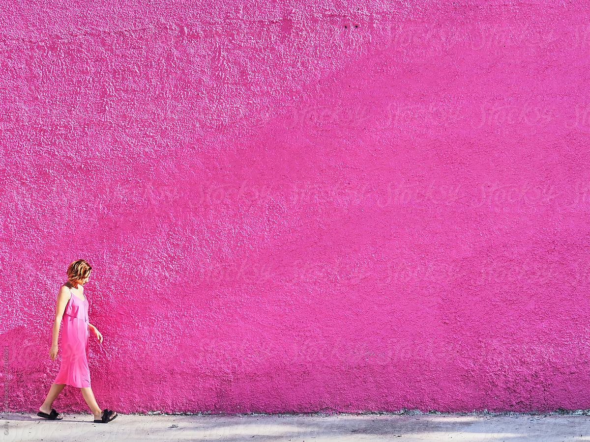 Woman in pink dress walking along pink building.