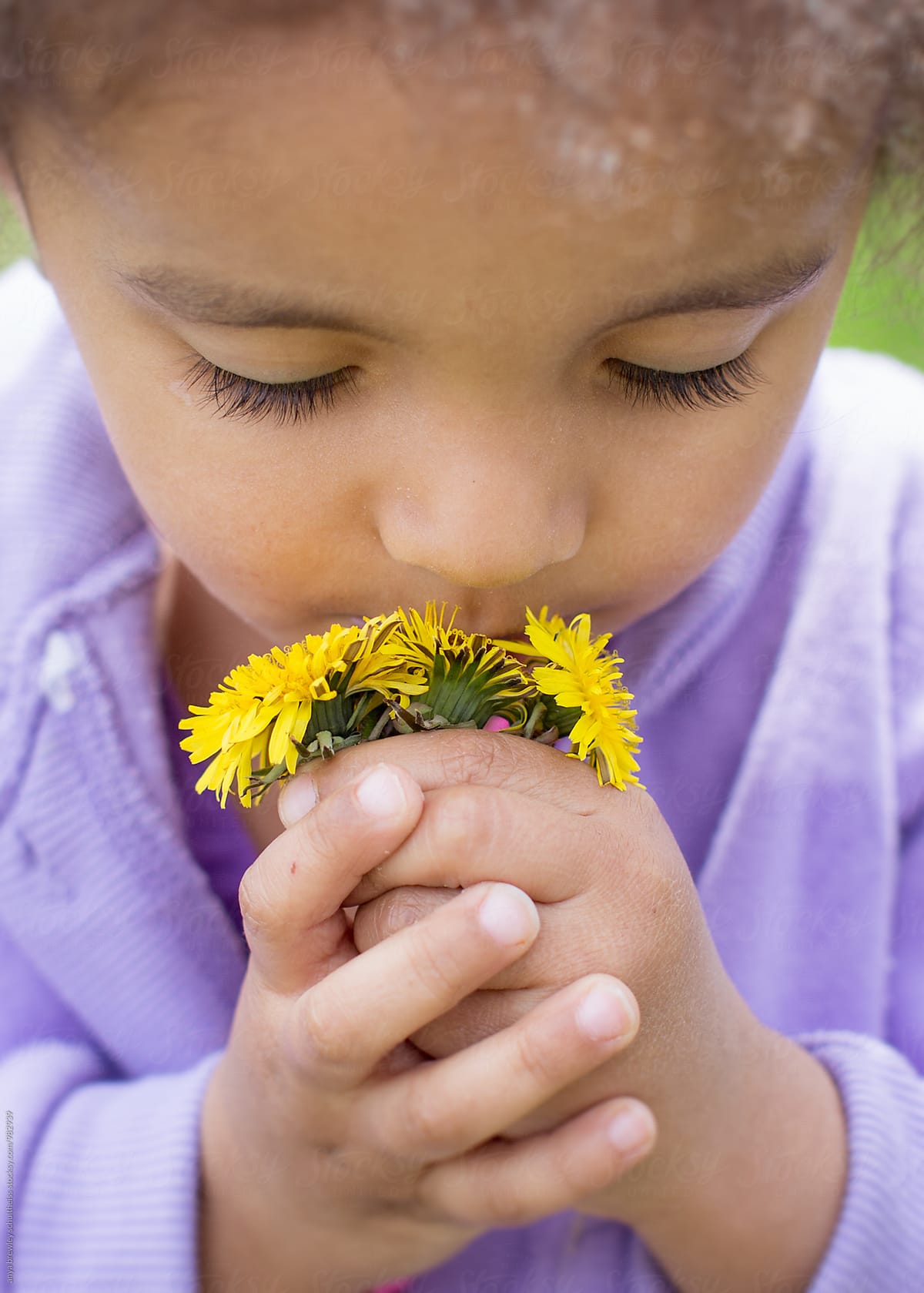 A young girl smelling a bundle of yellow dandelions