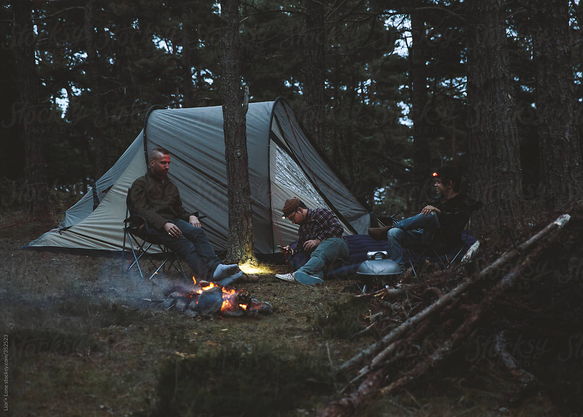 Three guys chilling in a campsite by the fire at night