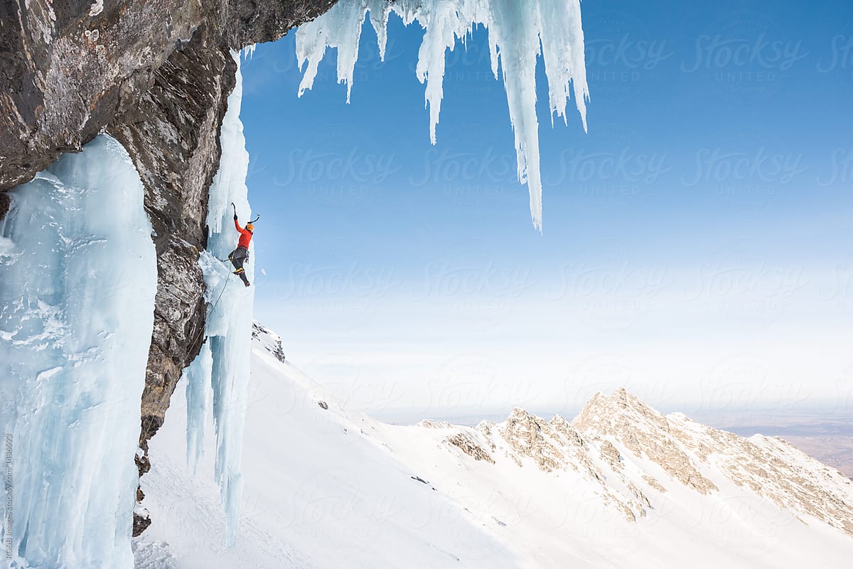 Anonymous man ice climbing on steep frozen waterfall in mountains