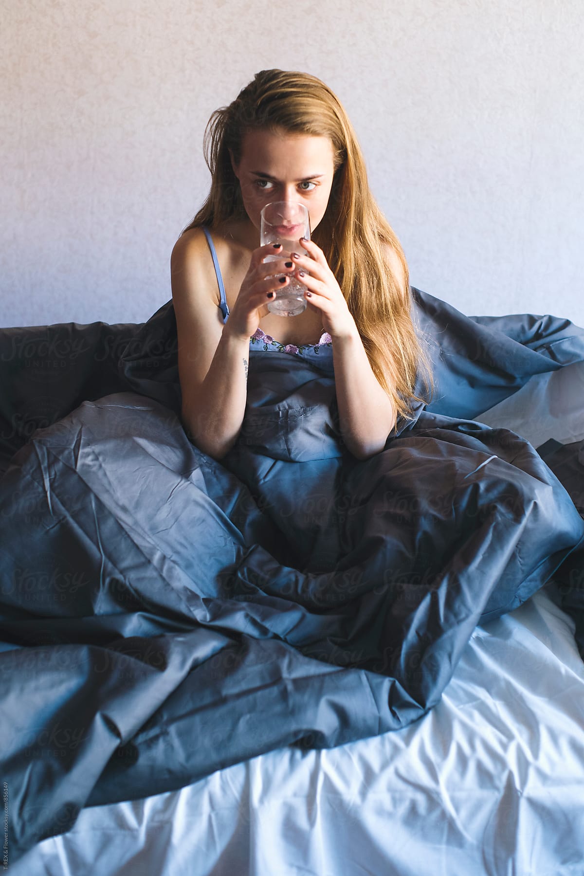 Portrait of sick young woman drinking water in bed