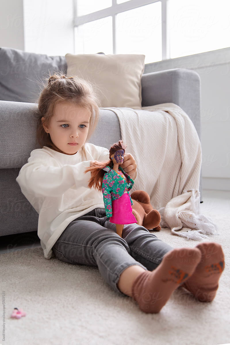 Cute girl playing with doll sitting on floor at home
