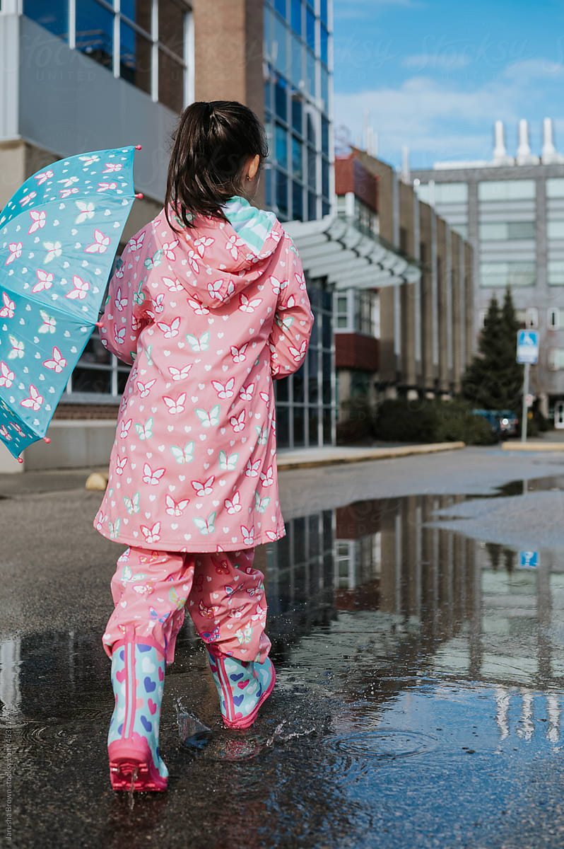 Young girl walks in a puddle with rain boots and an umbrella.