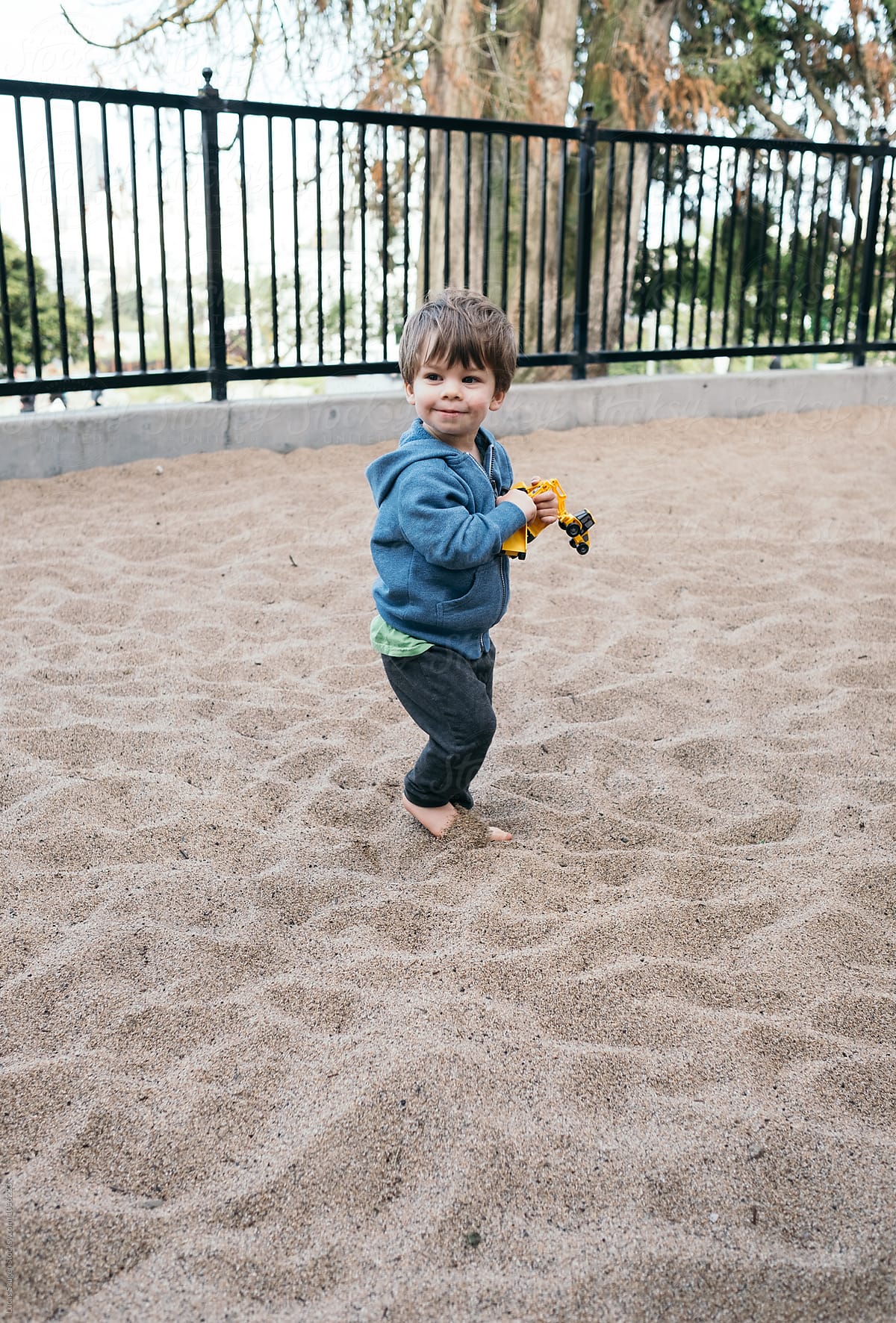 Young boy happy in a very large sand box with a small construction toy.
