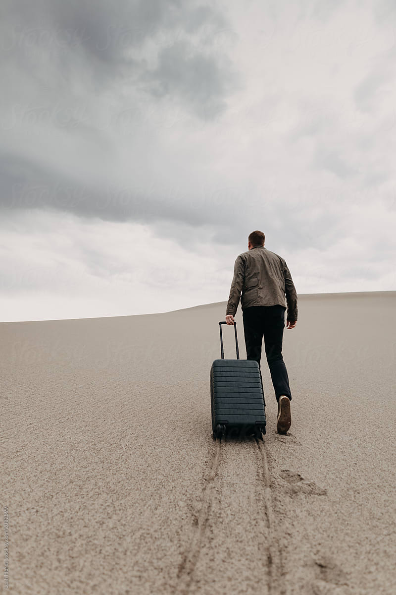 Man Walking Through Dunes Dragging Luggage