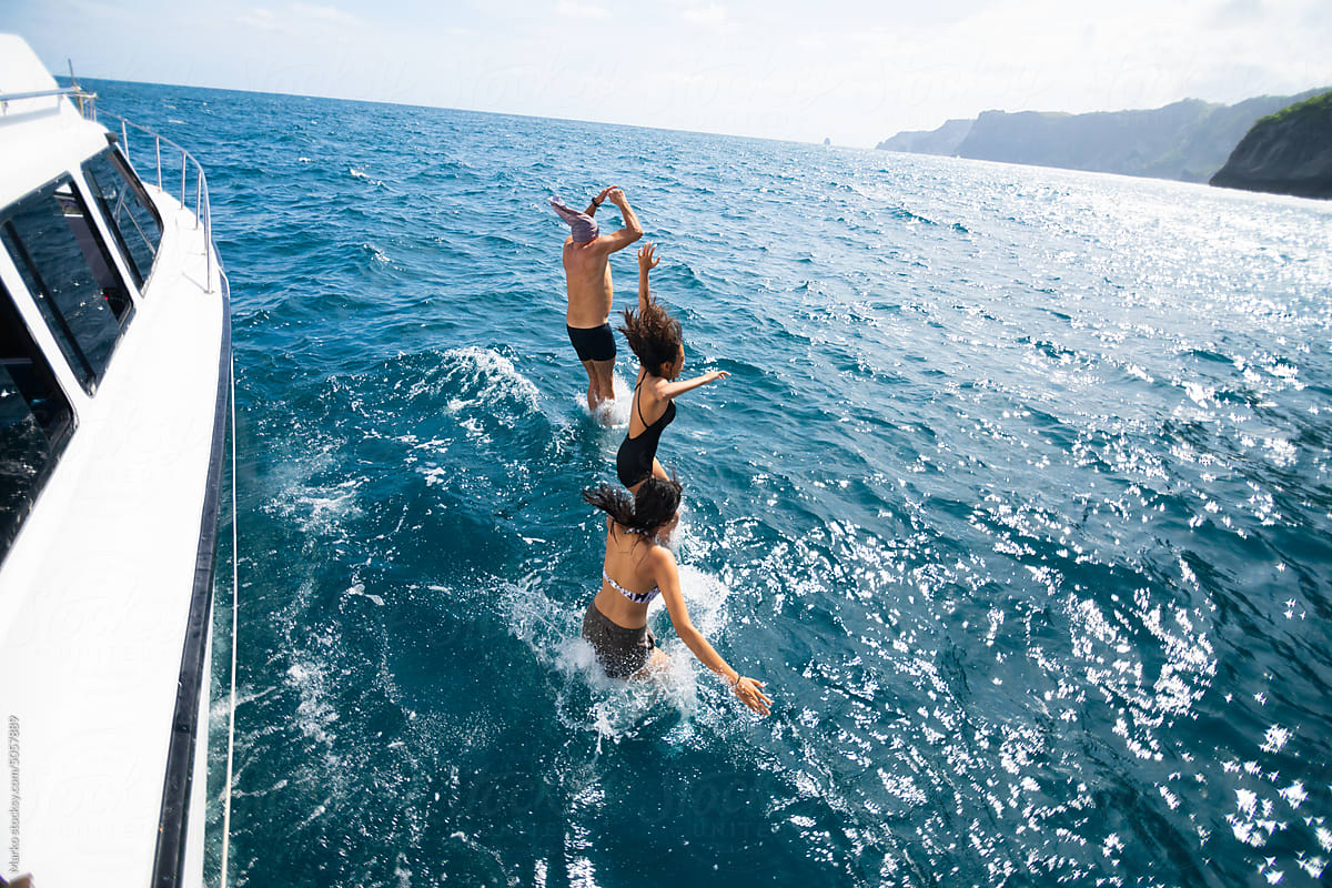 Happy people jumping off boat to ocean