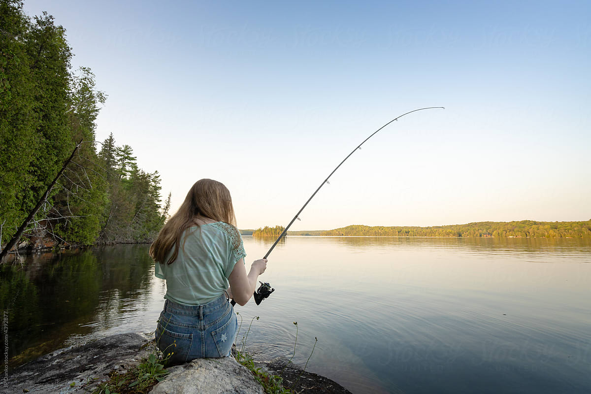 Girl Fishing Rod Sitting Rock Summer Lake Sunset by Stocksy