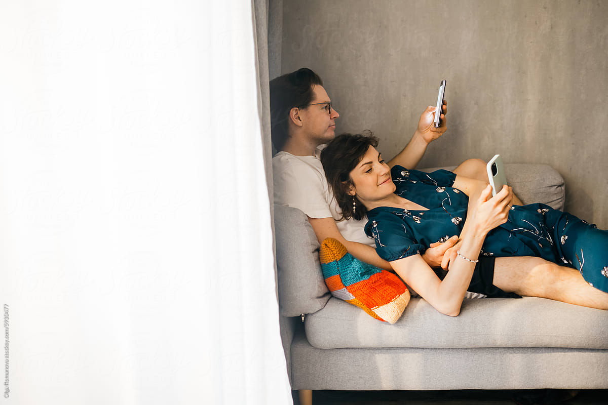 Smiling couple at home on the couch, both using their smartphones
