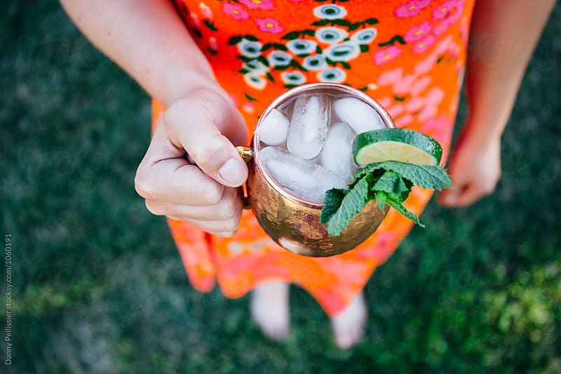 Woman holding Moscow Mule in red sun dress.