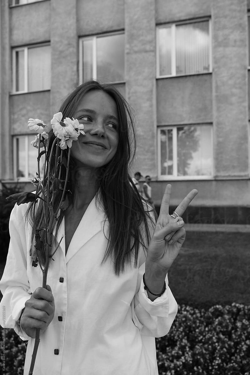 black and white portrait of a beautiful smiling girl holding flowers and showing a peace sign with her fingers at a peaceful protest for freedom in Belarus