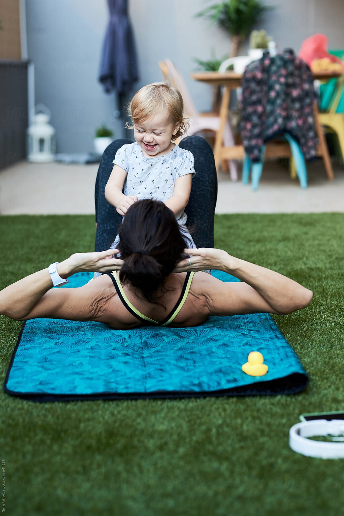 Baby sitting on mother doing abs exercise on mat.