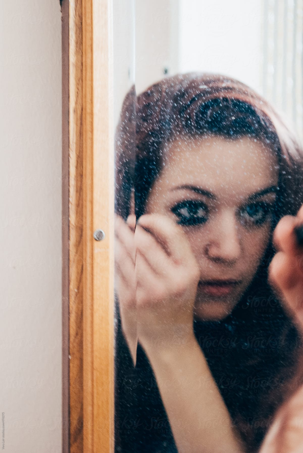 Reflection In A Mirror Of A Woman Applying Make Up By Stocksy