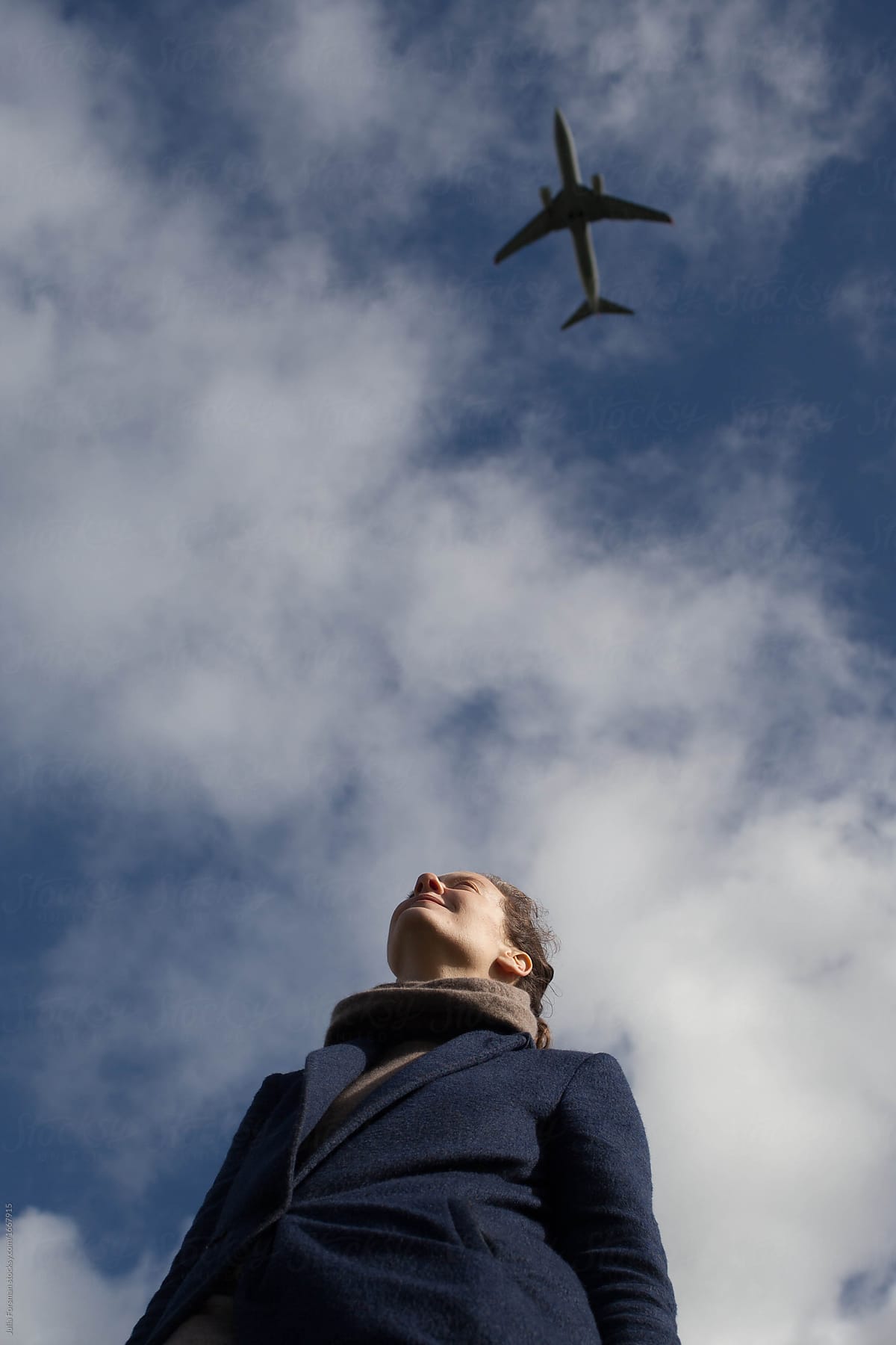 View of a woman from below with lots of sky and an aeroplane.