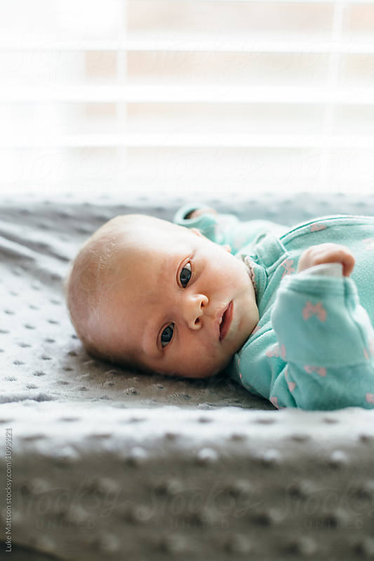 Newborn Baby Girl In Green Onesie Lying On Changing Table Looking At Camera