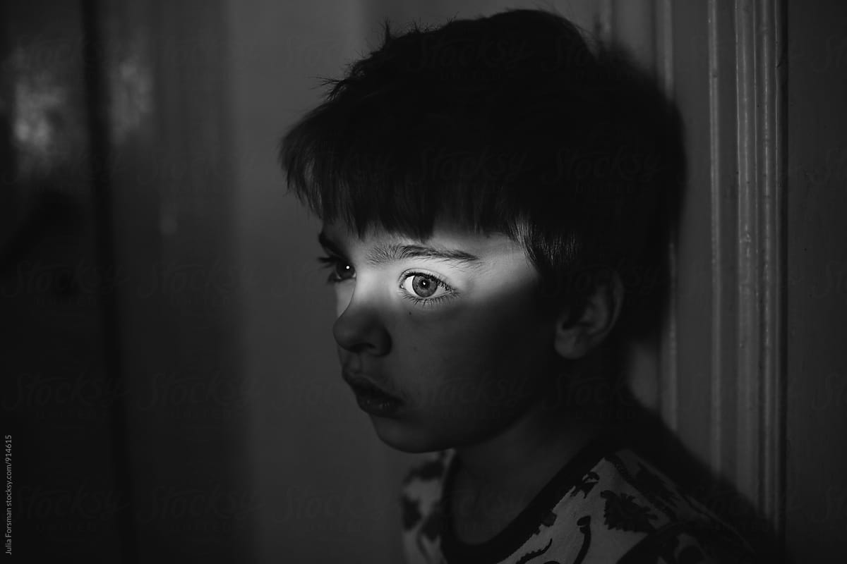 Black and white of boy in dark room with a bright strip of light across his eyes.