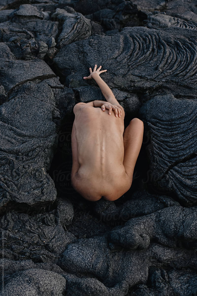 Naked woman sitting and stretching on black solid lava in Iceland