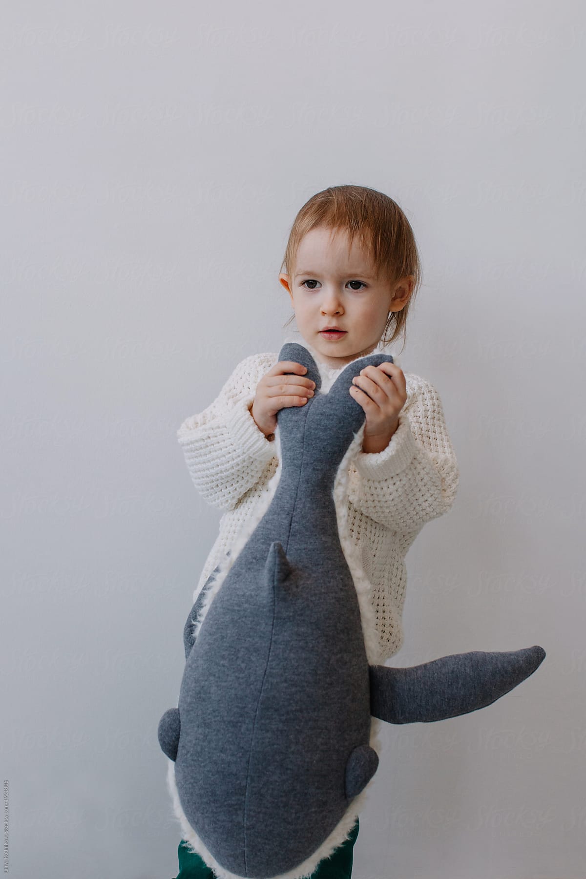 Lovely boy playing with plush whale by the white wall